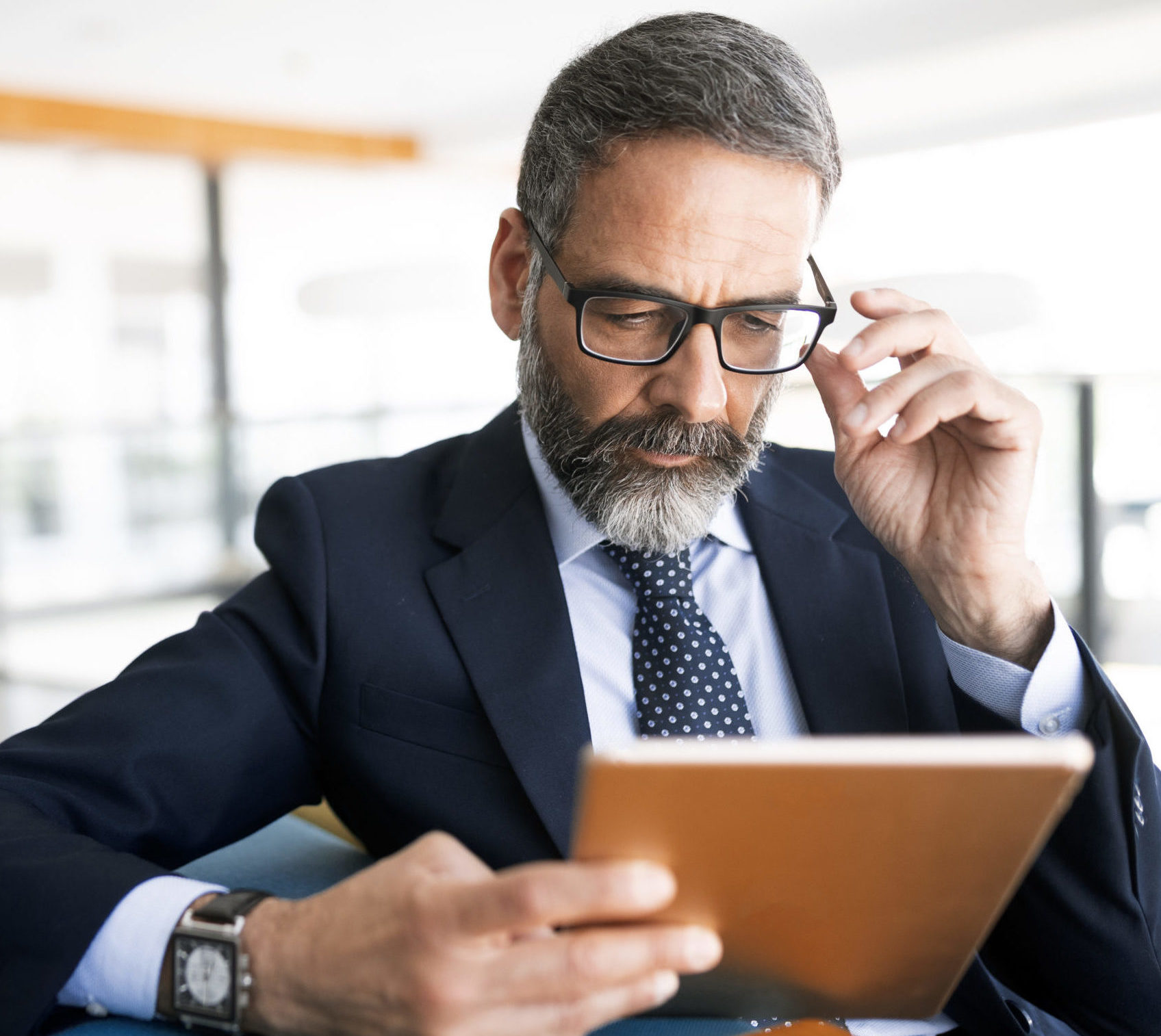 Male client executive sitting on an armchair reading a corporate sustainability report on a tablet